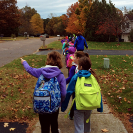 A group of students wearing backpacks walking to school on a sidewalk on an autumn day